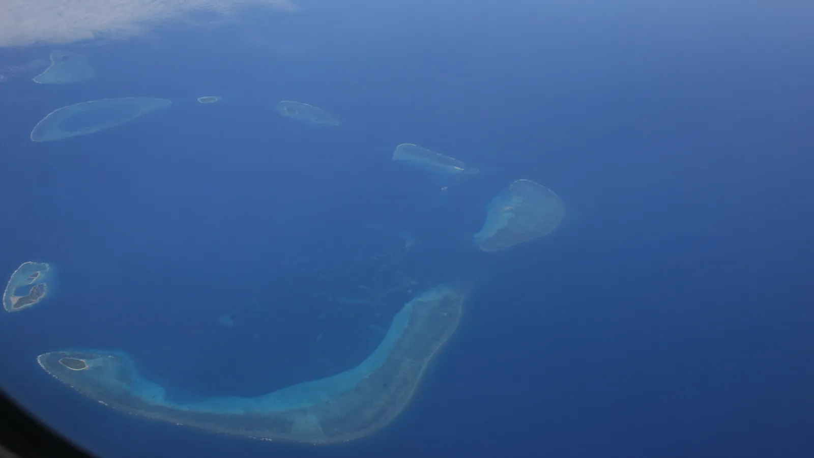 Aerial view of the Crescent Group of the Paracel Islands — low coral islets and reefs ringed by turquoise shallows in the South China Sea, seen from an airliner window.