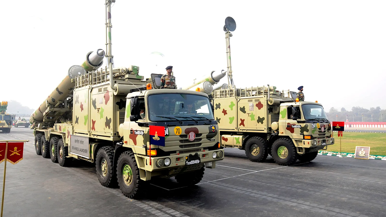 Two Indian Army BrahMos mobile autonomous launcher vehicles with missile canisters raised, crewed by soldiers during a parade.