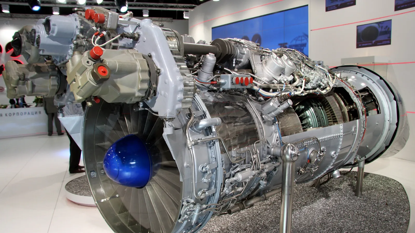 An AL-31FP thrust-vectoring turbofan engine for the Su-30MKI displayed on a stand, with its blue intake spinner and exposed accessory gearbox visible.