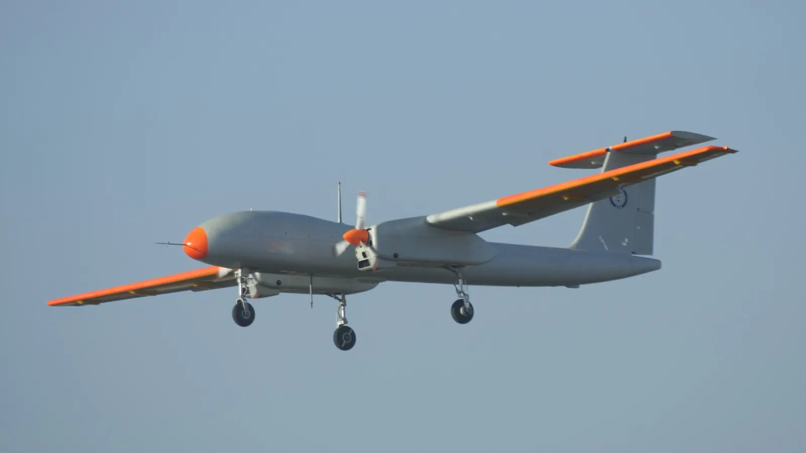 The DRDO TAPAS BH-201 medium-altitude long-endurance UAV in flight, a grey twin-boom drone with orange test markings on its nose and wingtips.
