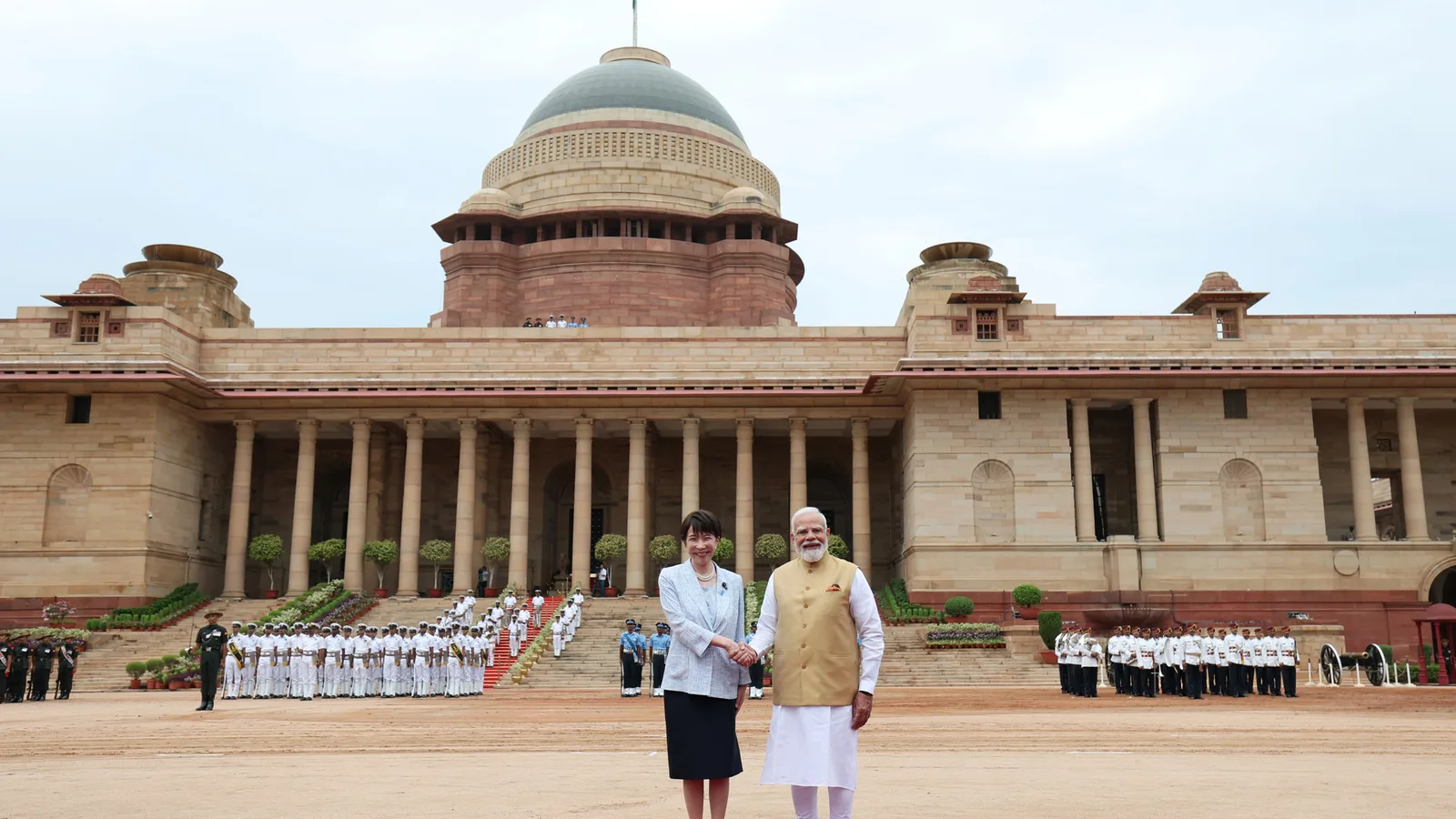 Prime Minister Narendra Modi shakes hands with Japanese Prime Minister Sanae Takaichi on the red carpet at Rashtrapati Bhavan, the honour guard and forecourt behind them.