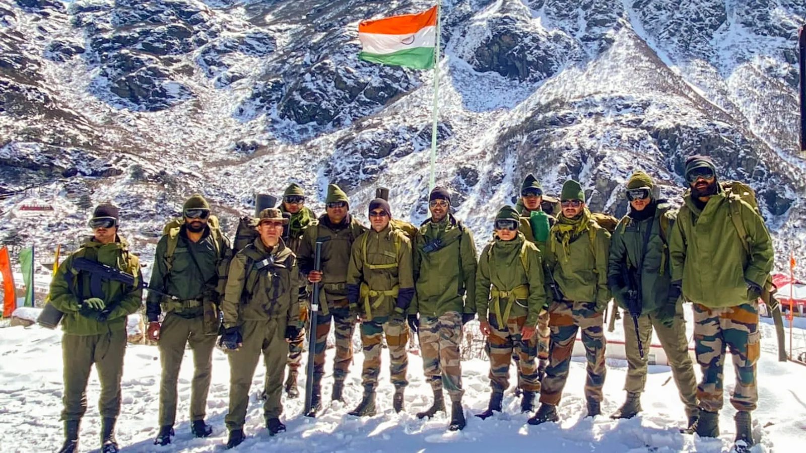 Indian Army soldiers in cold-weather gear stand in snow beneath the Indian flag at a high-altitude post in North Sikkim, with snow-covered Himalayan slopes behind them.