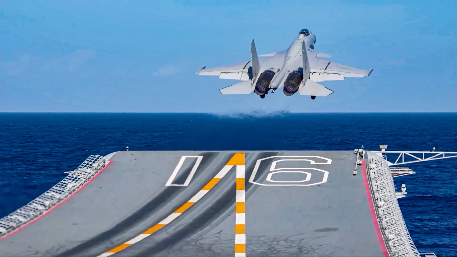 A J-15 carrier fighter climbs away from the ski-jump bow of the Chinese aircraft carrier Liaoning, whose hull number 16 is painted on the flight deck.