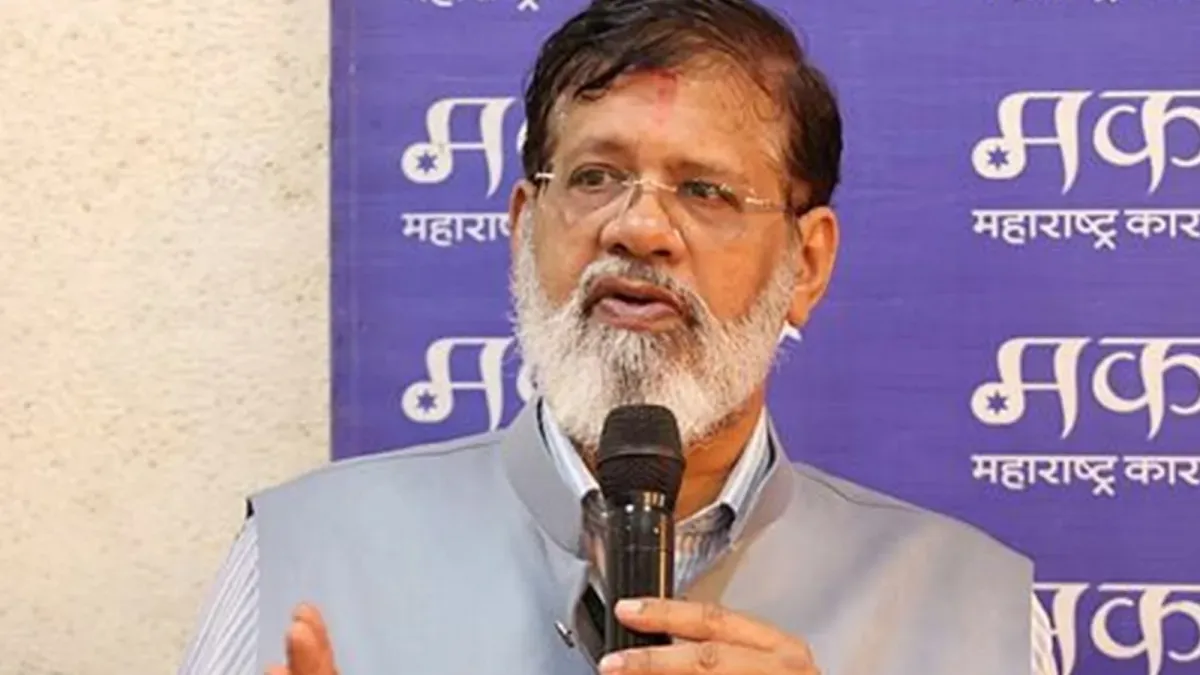 Pradeep Kurulkar, a bearded man wearing glasses and a grey jacket, speaks into a microphone at an event in front of a purple backdrop.