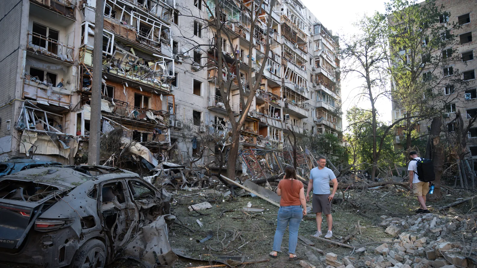 Residents stand among debris and burned-out cars in front of apartment buildings with blown-out windows and wrecked balconies in Kyiv after the Russian drone and missile attack.