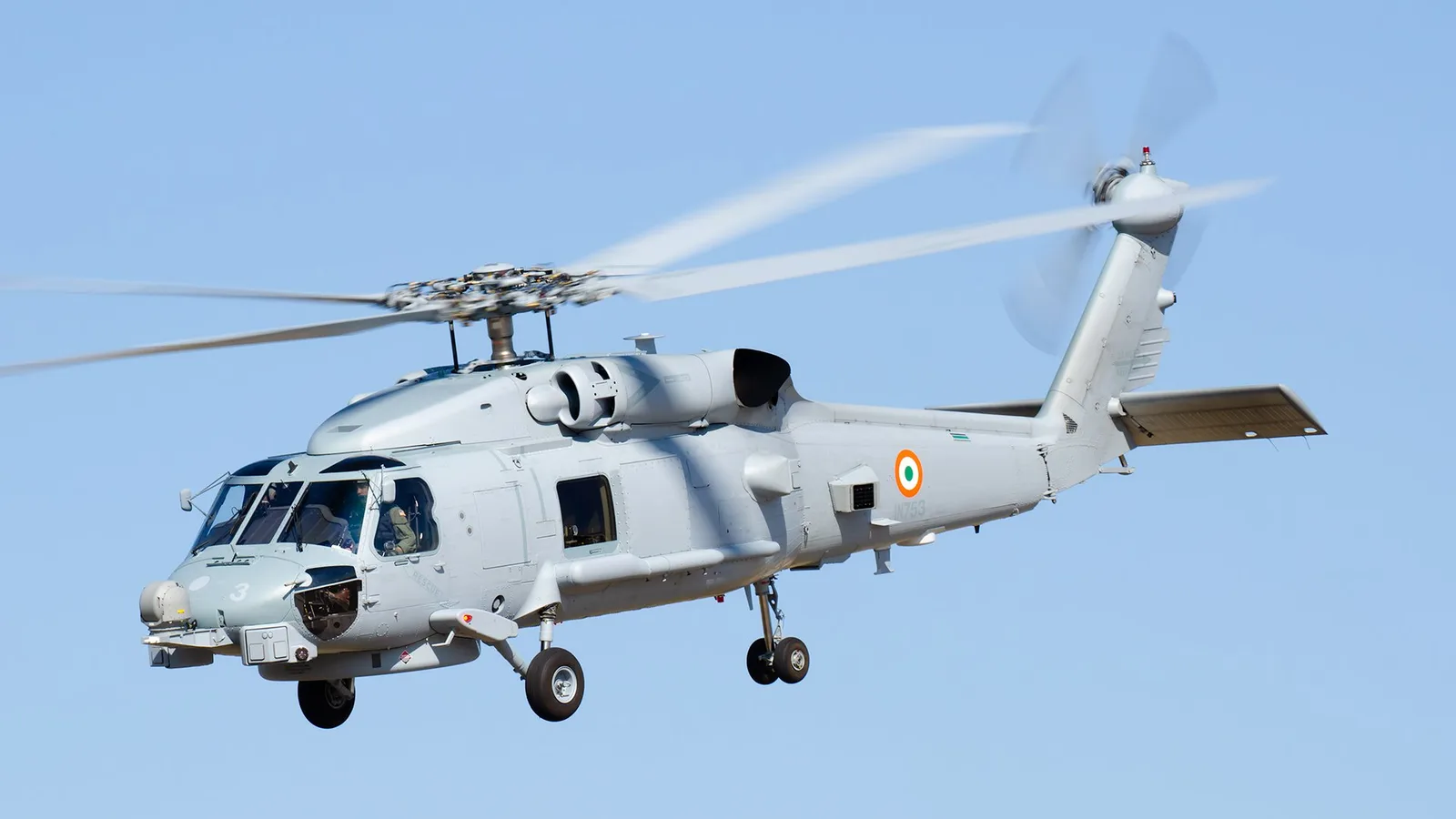 An Indian Navy MH-60R Seahawk helicopter in flight, roundel visible on the tail boom, landing gear extended.