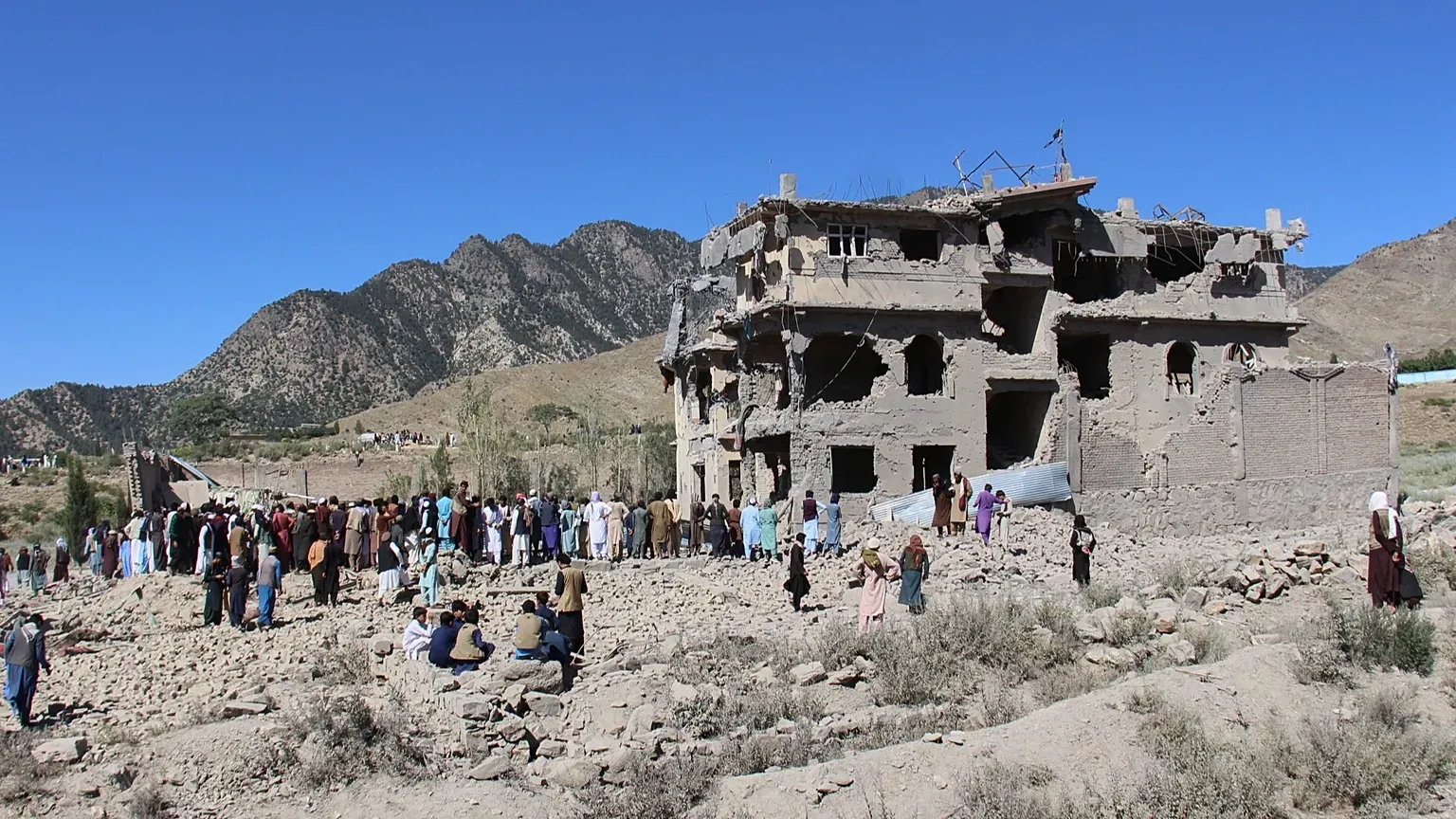 A crowd of residents gathers on rubble around a multi-storey building gutted by air strikes in a mountain-ringed valley in eastern Afghanistan.