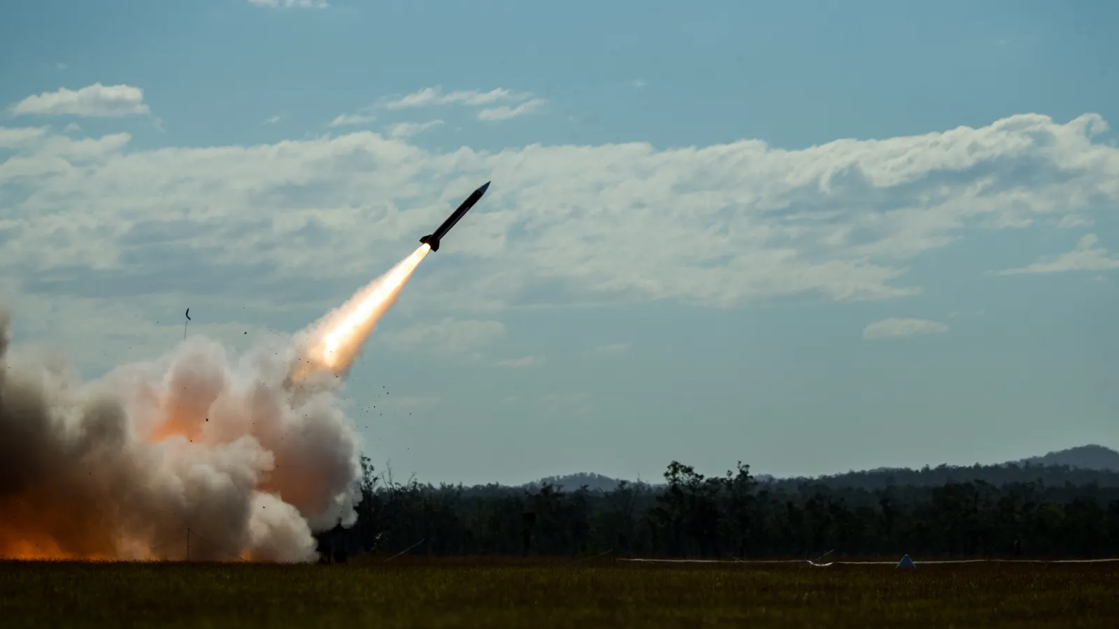 A Patriot interceptor missile climbs away from its launcher in a plume of flame and smoke during a live-fire exercise.