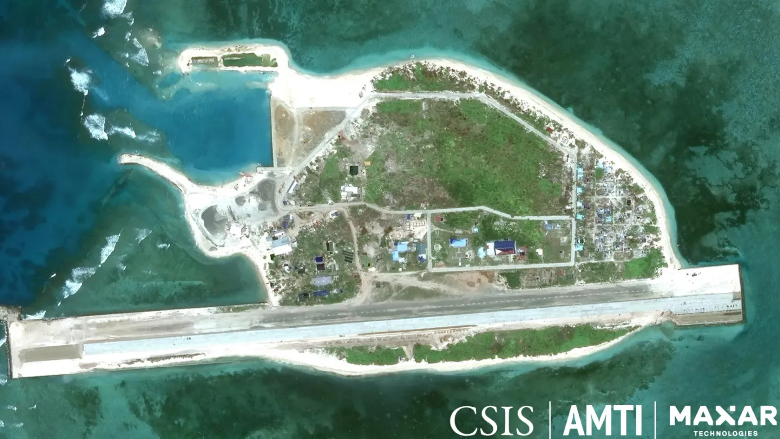 Satellite image of Thitu Island (Pag-asa) in the Spratly archipelago, showing its runway along the southern shore, a dredged harbour and clustered buildings amid surrounding reef.