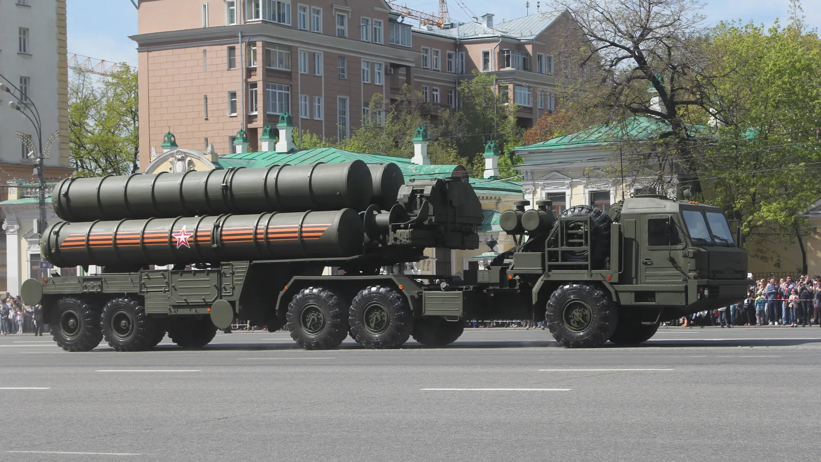 An S-400 Triumf transporter-erector-launcher carrying four missile tubes on its eight-wheeled chassis drives down a city avenue during a parade.