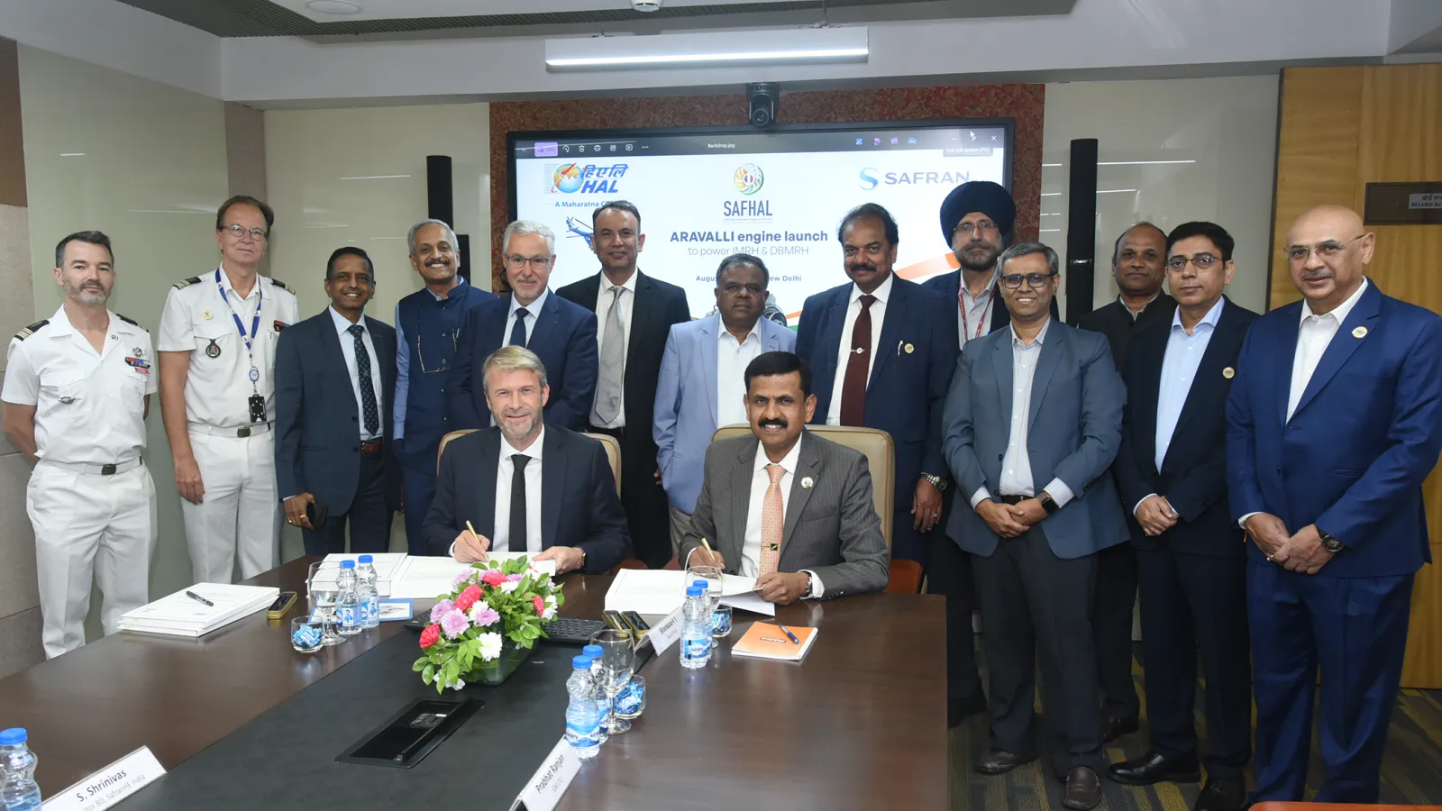 A Safran Helicopter Engines executive and an HAL executive seated at a boardroom table signing the SAFHAL Aravalli engine contract in New Delhi on 26 August 2026, with HAL, SAFHAL and Safran officials standing behind them in front of a screen showing the three companies' logos and the words 'Aravalli engine launch'.