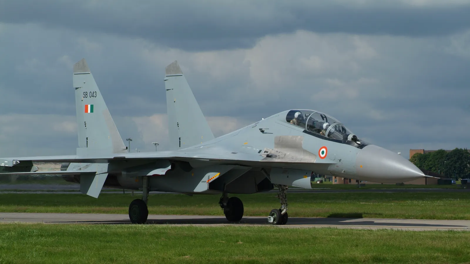 An Indian Air Force Su-30MKI fighter, serial SB 043, with tricolour fin flash and roundel, taxiing on a runway with its two-man crew in the cockpit under an overcast sky.