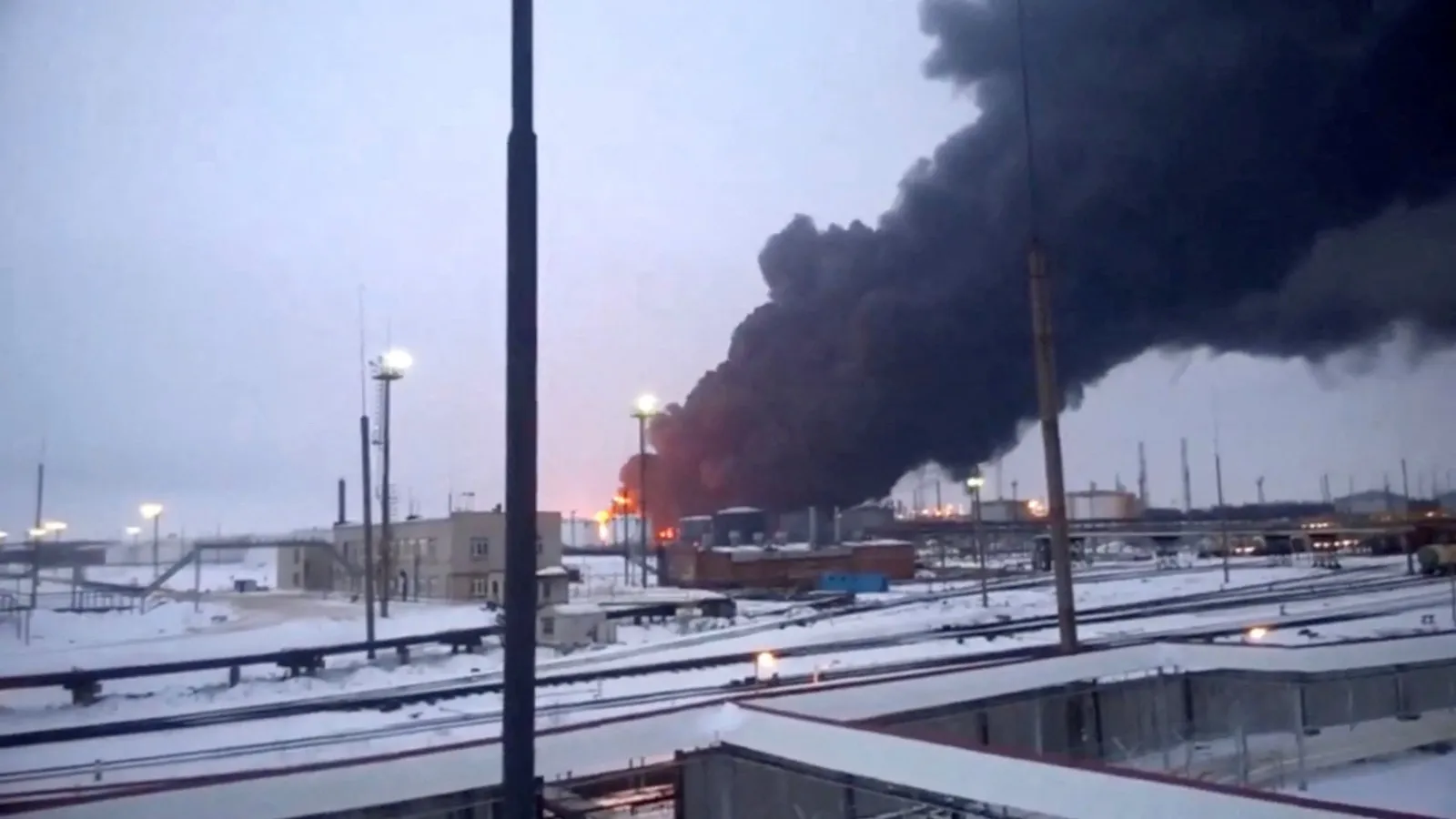 Thick black smoke billowing over a snow-covered Russian oil refinery burning after a Ukrainian drone strike.